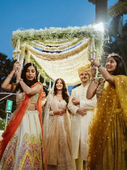 The bride's joyful entrance under the phoolon ki chadar, surrounded by smiling friends and family.