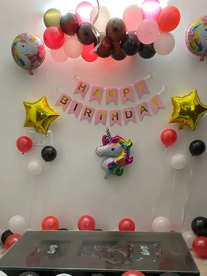 A simple unicorn-themed birthday setup at home. The decoration includes a "Happy Birthday" banner, a unicorn foil balloon, and balloons scattered on the floor.