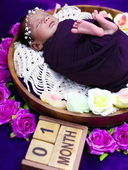 A side view of a one-month-old baby girl in a basket surrounded by flowers, showing the pearl headband and peaceful sleep.