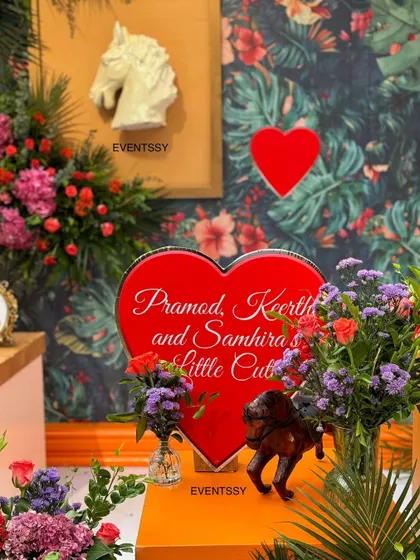 A personalized heart-shaped sign with the parents' names, set amongst lush flowers.