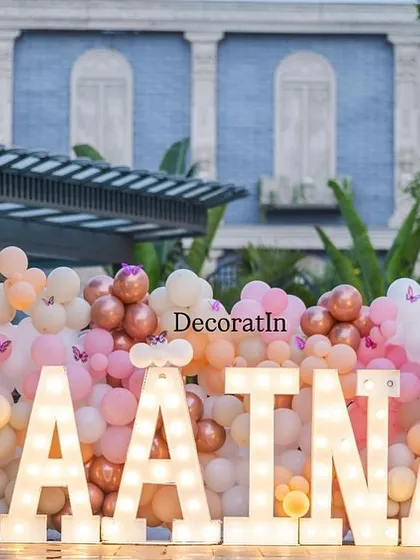 A daytime shot of the "RAATNA" marquee letters, showing the soft pastel colors of the balloon wall and the detailed butterfly cutouts.