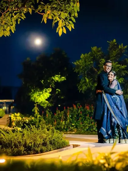 A romantic night portrait of a couple in a garden, with the full moon watching over them. This wide shot captures the serene and magical ambiance.