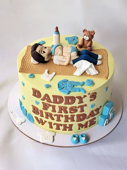 A cake to celebrate a daddy's first birthday with his new baby. The design shows them napping together, surrounded by baby items.
