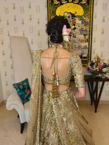 A full back view of the bride, showing how the messy bun with pink lilies complements her gold sequined lehenga and backless blouse design.