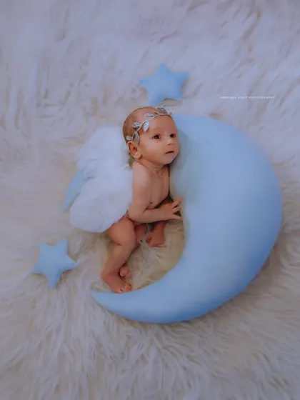 A slightly different angle of the angelic moon theme, this shot captures the newborn in a peaceful, alert state. The soft lighting and fluffy textures create a serene and heavenly atmosphere for this baby portrait.