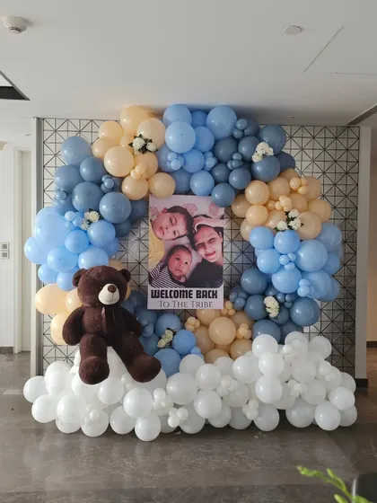 Make your welcome home celebration deeply personal with a custom photo display. This beautiful balloon arrangement in shades of blue, peach, and white frames a personalized poster featuring the family's photos, creating a heartwarming focal point to welcome the new baby.