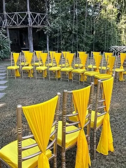 Seating arrangement for an outdoor Haldi function, with chairs decorated with yellow drapes to match the overall theme.