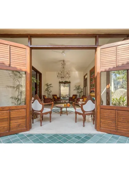 Large, traditional wooden doors open up to connect the living room with an outdoor patio. This design feature allows for natural ventilation and creates a seamless flow between indoor and outdoor living spaces.