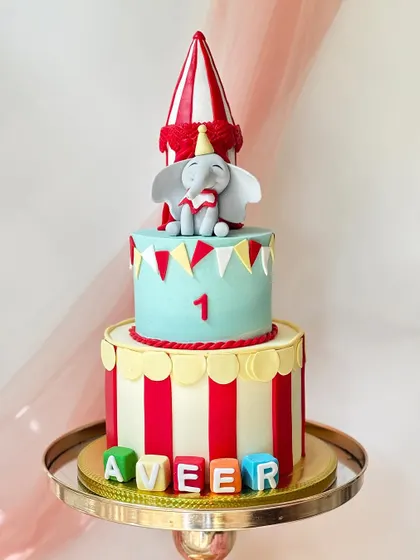 Another take on the circus theme, this two-tiered cake features Dumbo on top of a red-and-white striped tent. The base includes alphabet blocks to spell out a name.