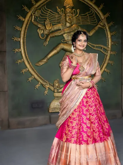A full-length shot of this beautiful half-saree look. The makeup is designed to complement the vibrant colors of her outfit and the traditional setting.