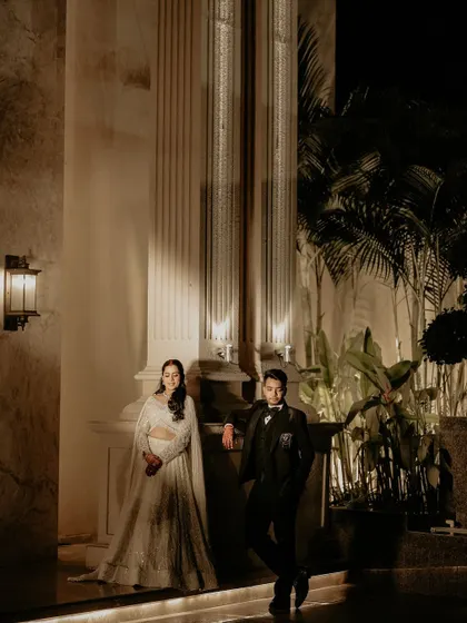 A stylish portrait of the couple against a grand, pillared backdrop. The night lighting and their confident poses give this Sangeet photo a touch of modern royalty.