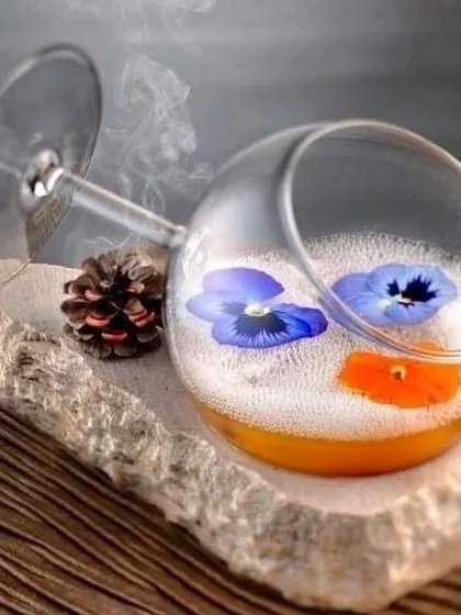 A drink that is also a piece of art. This cocktail is presented in a tilted glass, resting on a stone, with edible flowers floating on the foam.