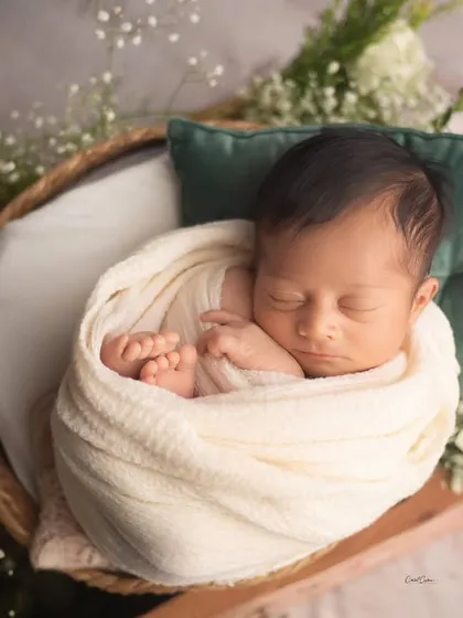 Simplicity at its best. This baby is sleeping peacefully in a basket, wrapped in a cream swaddle with just a hint of greenery and a soft pillow for support.