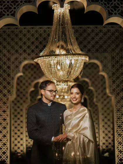 An elegant portrait of the couple at their reception. The grand chandelier and intricately patterned backdrop create a luxurious and timeless setting.