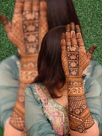 A beautiful shot of a bride's full-arm mehndi, featuring intricate bands of lotus flowers and geometric patterns.