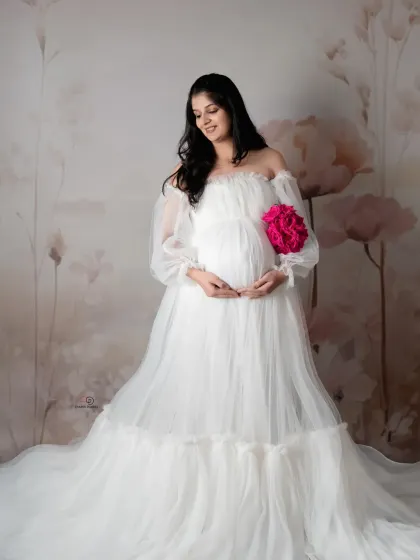 An angelic portrait in a white tulle gown against a soft, painted floral backdrop. Holding a pop of color with the pink flowers adds a sweet touch to this delicate maternity photo.