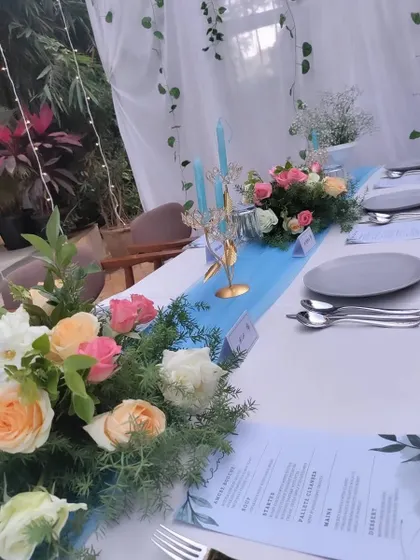 An elegant candlelight dinner setup for an intimate celebration. The table is decorated with a blue runner, fresh rose bouquets, and tall candles.