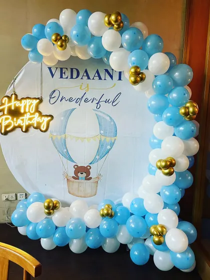 A special hot air balloon adventure theme for a first birthday. The custom backdrop features a cute teddy bear, and the blue and white balloon arch is accented with gold balloons to look like clouds in the sky.