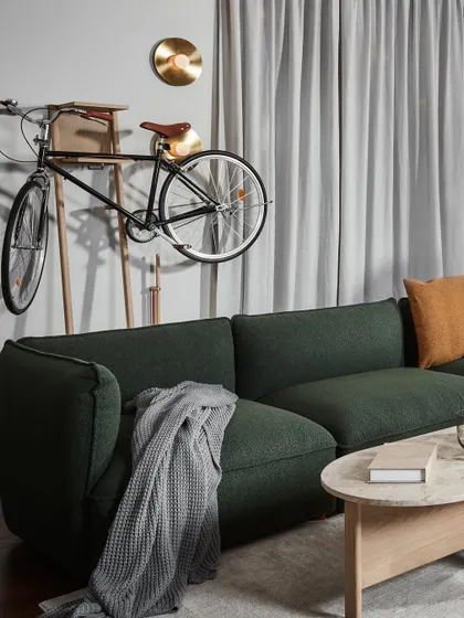 The Copenhang sectional sofa in a deep green, creating a cozy and stylish corner. The addition of a bicycle as wall art speaks to the urban, hipster-inspired culture behind this collection, blending lifestyle and design.