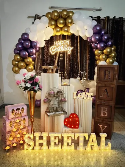 A lovely birthday setup for Sheetal, featuring a purple, white, and gold balloon arch, 'BABY' blocks, and personalized marquee letters.