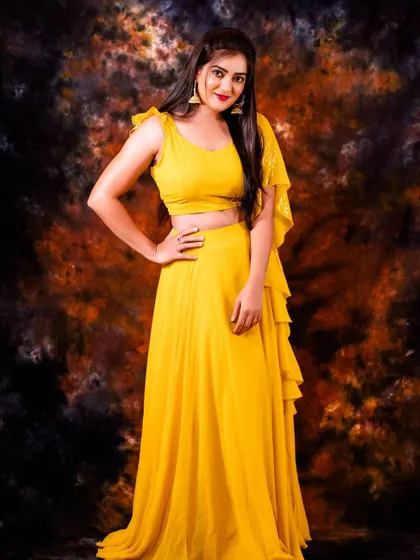 A vibrant studio portrait in a bright yellow lehenga. The dramatic, dark backdrop makes the color pop, creating a high-energy and celebratory image.