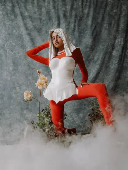 A look from the 'ASTRID' editorial featuring a white breastplate made from Plaster of Paris. The styling contrasts a fiery red bodysuit with the pure white armor, set in a misty, dreamlike environment.