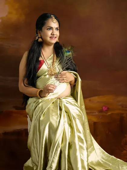 A regal portrait of a mom-to-be in a light green silk saree, holding a peacock feather, symbolizing beauty and new life.