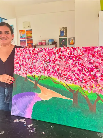 A participant proudly stands next to her large, vibrant painting of cherry blossom trees.
