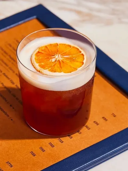 A classic whiskey sour, with a perfect foam top and a dehydrated orange wheel garnish, resting on our menu.
