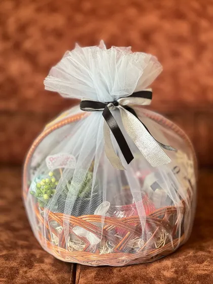 A lovely birthday gift hamper in a wicker basket. It's wrapped in light blue net with a classic black and silver ribbon, filled with a surprise selection of treats.