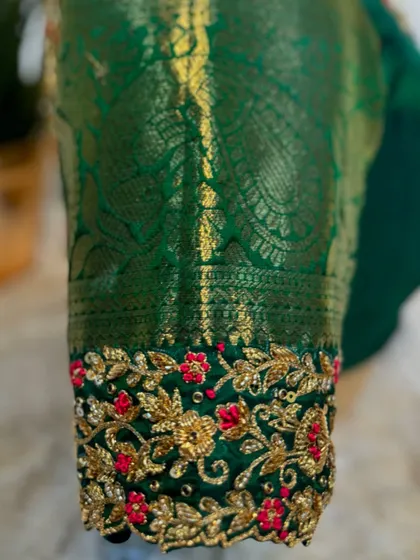 A detailed shot of the sleeve cuff, highlighting the intricate red floral motifs against the gold zari background.