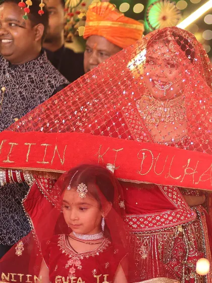The bride makes her grand entrance under a decorated phoolon ki chadar, with a custom banner proclaiming her as 'Nitin ki Dulhan', a beautiful and personal touch.
