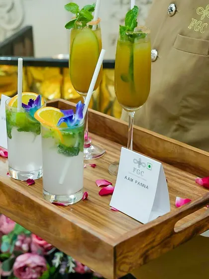 A server presents a tray of refreshing mocktails, including Aam Panna. The drinks are garnished with fresh mint, fruit slices, and edible flowers, demonstrating our commitment to beautiful presentation in every detail.