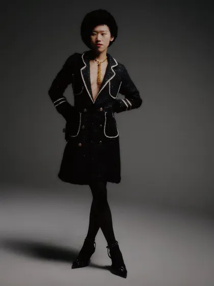 A full-length shot that captures the entire look, including the sheer tights and pointed heels. The composition is classic fashion photography, emphasizing the long lines of the silhouette.