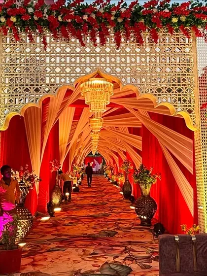 This royal entrance features a stunning arched gateway with intricate lattice work. The warm lighting inside the fabric tunnel creates a welcoming glow for arriving guests.