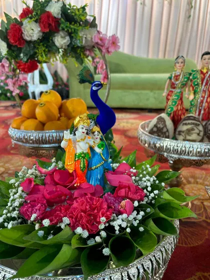 A centerpiece featuring a Radha-Krishna idol, surrounded by fresh flowers and peacock figures.