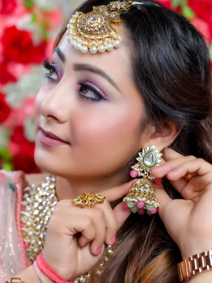 A close-up of a bride-to-be adjusting her beautiful jhumka earring. This shot is perfect for showcasing the details of the jewelry and makeup for an engagement or sangeet.