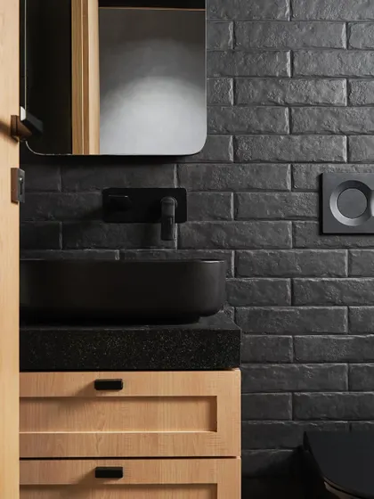 The guest bathroom at Zen House features a dramatic black brick-tile wall. This textural element is paired with a simple wood vanity and matte black fixtures for a moody, sophisticated look.