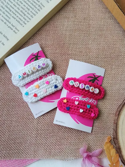 Our personalized name clips displayed on a rustic background. This set includes a white clip for "Amirah" and a pink one for "Husna".