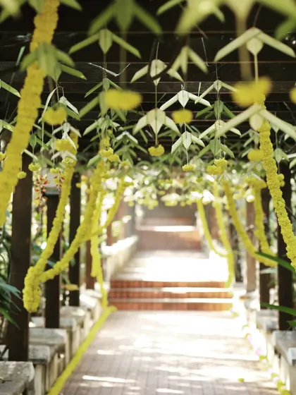 An outdoor walkway decorated with hanging yellow flower garlands and traditional woven leaf elements.