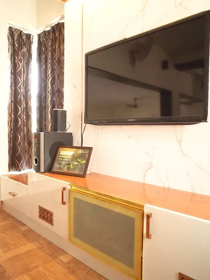 A close-up of the TV unit, featuring a white marble-finish console with unique brass handles and decorative vents. The design is both modern and detailed.