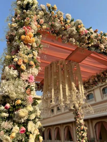 A lush floral archway from a Jodhpur wedding, overflowing with coral and peach roses, setting a romantic tone for the ceremony.