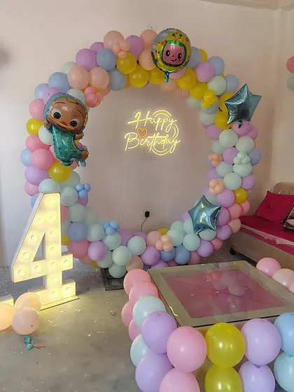 A pastel-themed 14th birthday with a Cocomelon touch. This home setup features a beautiful ring of pastel balloons, a neon sign, and large marquee numbers, showing how we can adapt themes for older kids too.