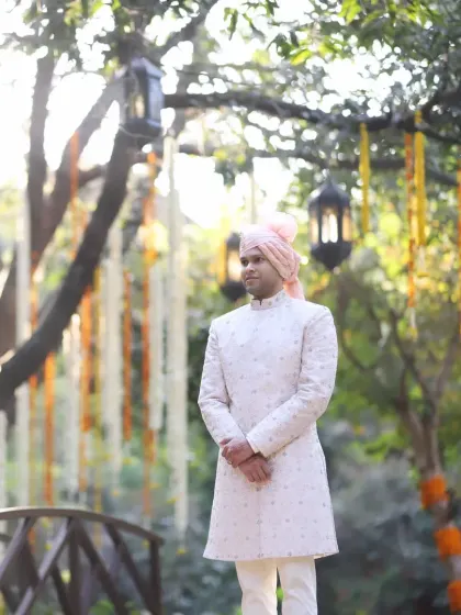 The groom awaits his bride, standing elegantly in a serene garden setting at the Taj Corbett, with floral hangings adding to the romantic atmosphere.