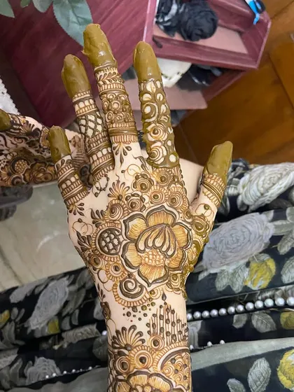 A close-up of a fresh Arabic henna design with a large central flower on the palm.
