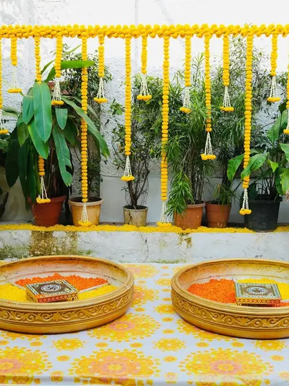 A simple and elegant haldi decor setup for an intimate home ceremony. The focus is on clean lines, traditional elements like marigolds, and a beautiful printed tablecloth.