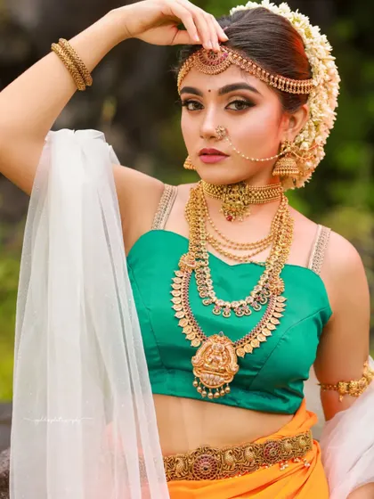 Inspired by the grandeur of Bahubali, this "Sakhi" look features a model in a unique orange and green dhoti-style saree. The outdoor setting and regal jewelry complete the ancient princess aesthetic.