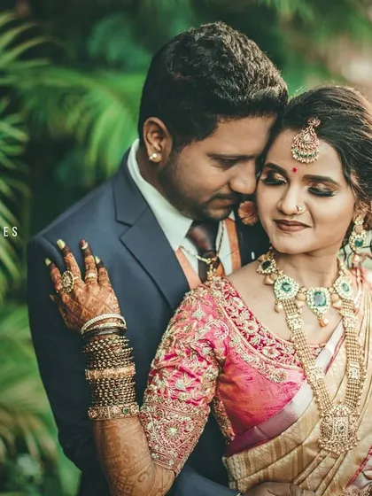 A couple shares a warm embrace outdoors, dressed in their reception attire. The lush green background provides a beautiful contrast to their formal outfits.