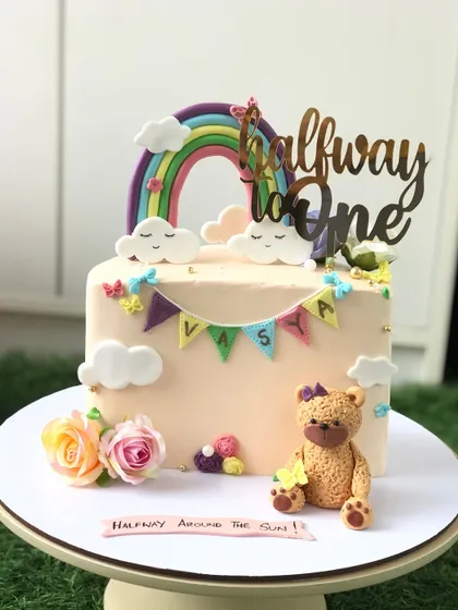 A "Halfway to One" cake for a six-month celebration. This design features a cute teddy bear, a pastel rainbow, and a little name banner.