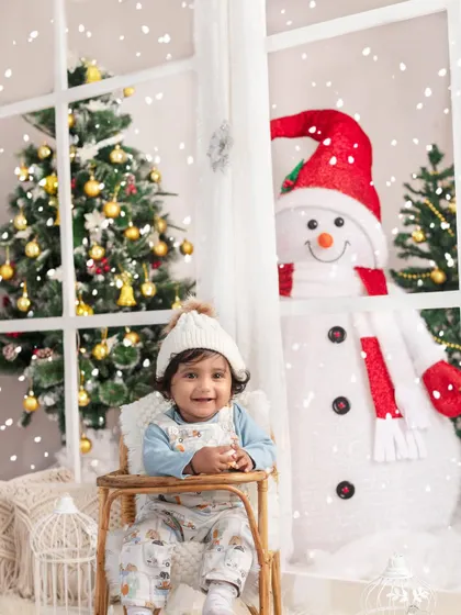 A happy baby enjoying the magical snowfall from a cozy chair, with our friendly snowman peeking through the window.